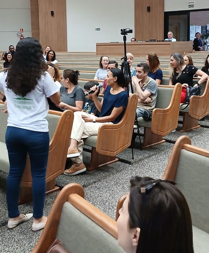 Voluntária conversando com participantes na plateia do auditório
